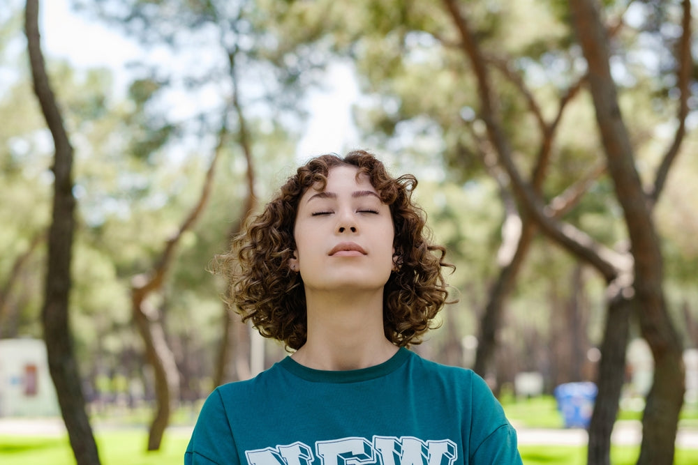 A young woman stands in a park and inhales. 