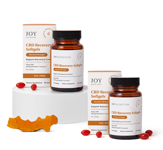 Two amber glass bottles of CBD Recovery Softgels with orange and white boxes, red capsules, and turmeric root displayed on wh